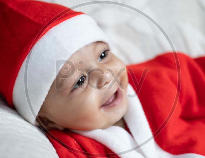 Portrait Of Baby Smiling In Santa Costume With Tree In Background