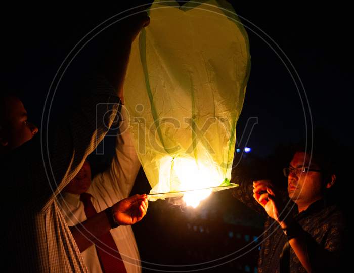 People Holding A Yellow Sky Lantern With The Flames Showing Clearly