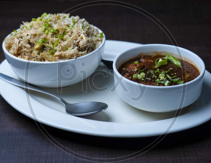 Fried rice with chicken, chicken manchurian garnished with spring onions. Prepared and served in a white plate. wood texture in the background