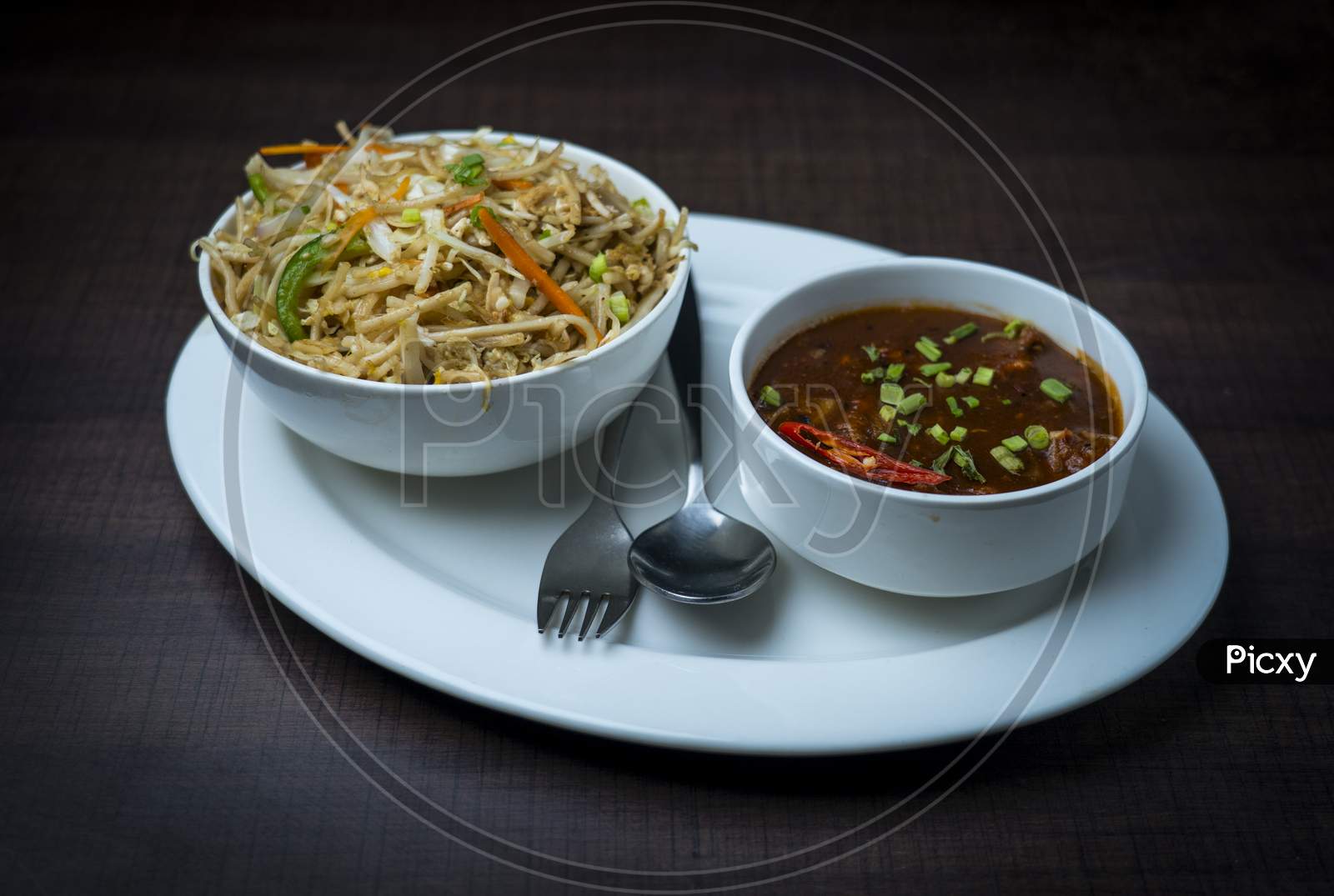 Chinese noodles with chicken, chicken manchurian garnished with spring onions. Prepared and served in a white plate.  wood texture in the background