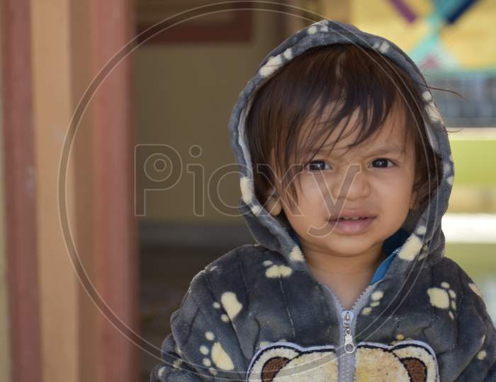 : A shallow focus of a cute Indian kid wearing a jacket with a bear in a house
