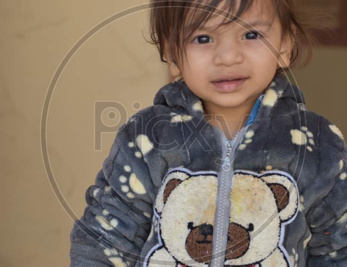 : A shallow focus of a cute Indian kid wearing a jacket with a bear in a house