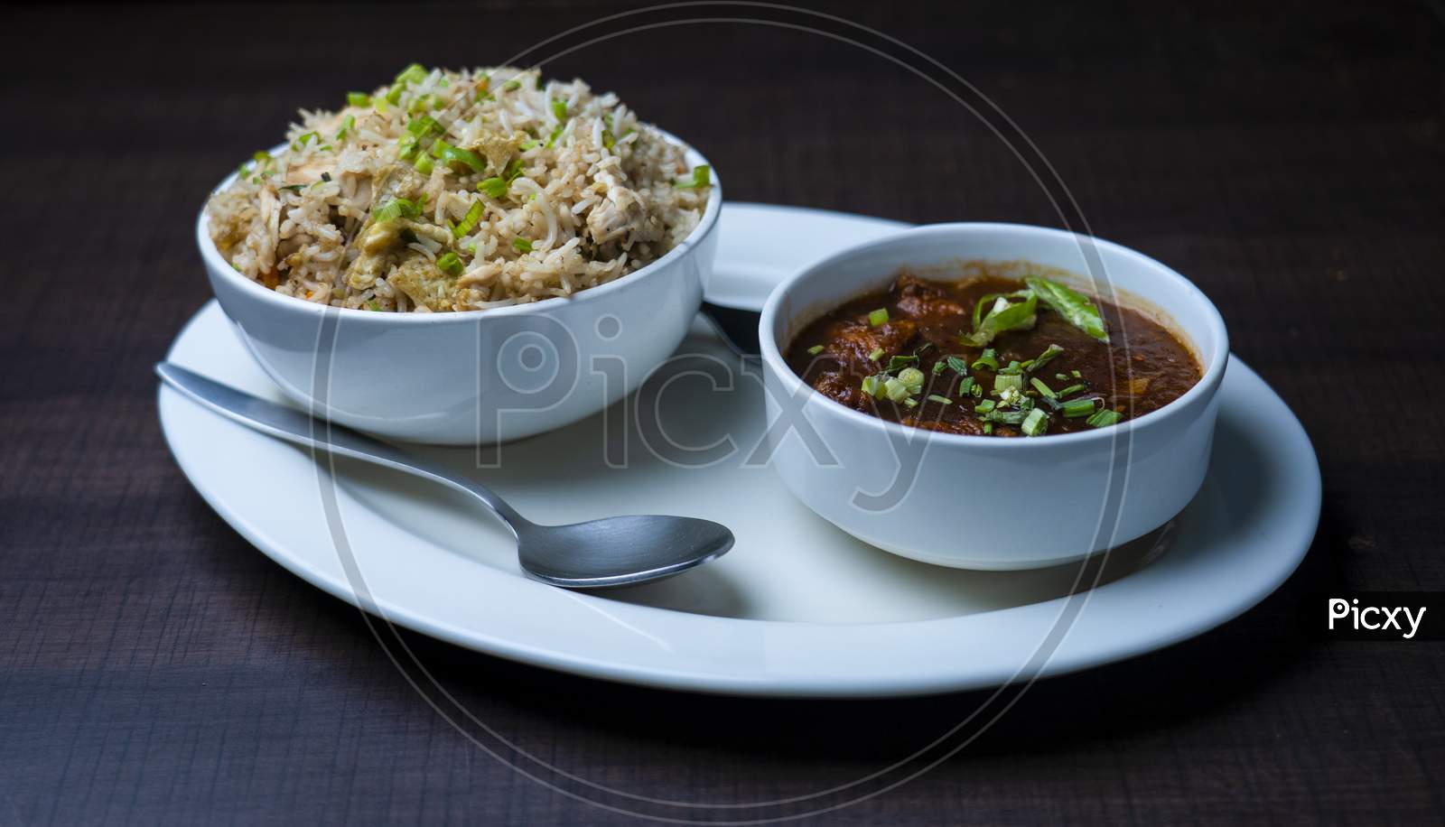 Fried rice with chicken, chicken manchurian garnished with spring onions. Prepared and served in a white plate. wood texture in the background