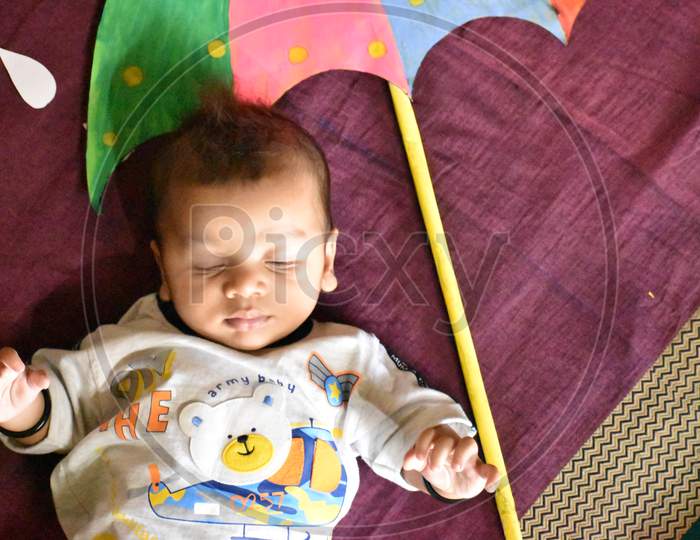 Adorable Indian child lying on a bed with an umbrella toy on it