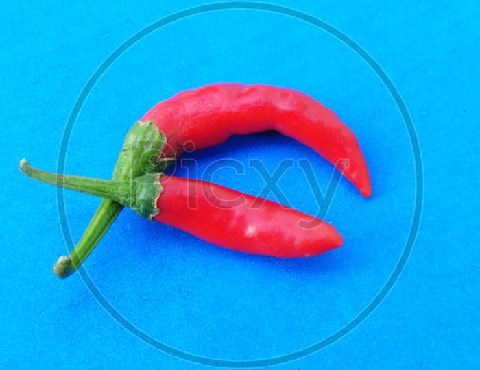 Top View Of Spicy Red Chili Peppers On Blue Background With Copy Space.