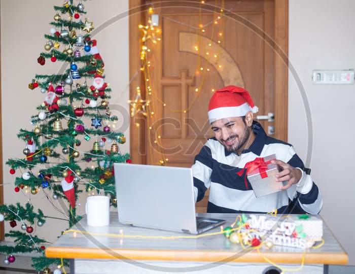 Christmas Celebration 2020, Young Man Congratulating Virtually Online On Laptop Computer Showing Gift Present, Pandemic, New Year, Holiday,Winter,December,New Normal.