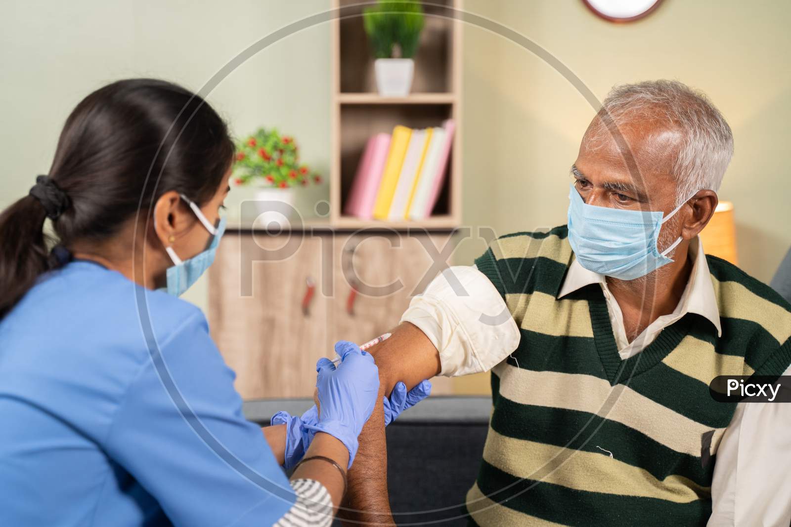 Doctor Giving Vaccination Shot To Elderly Patient By Syringe Or Injunction At Home While Both Worj Face Mask - Concept Of Home Health Check To Seniors During Coronavirus Covid-19 Pandemic.