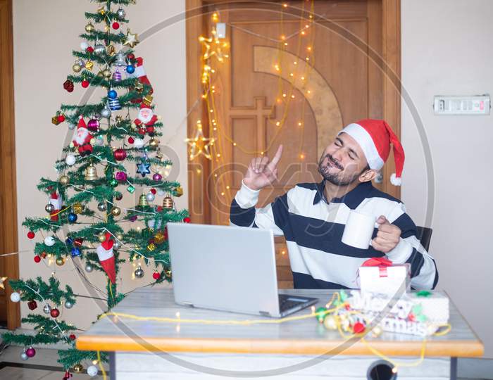 Cheerful Young Man Celebrating Christmas At Home During Pandemic, Sitting In Front Of Laptop Computer Online Virtual Conference, Enjoy Holiday Season, Shopping.