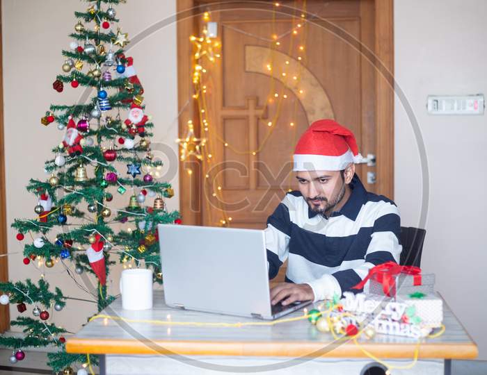 Young Indian Man Using Laptop Computer During Christmas Holidays, Work From Home During Pandemic, Winter,December,New Normal.