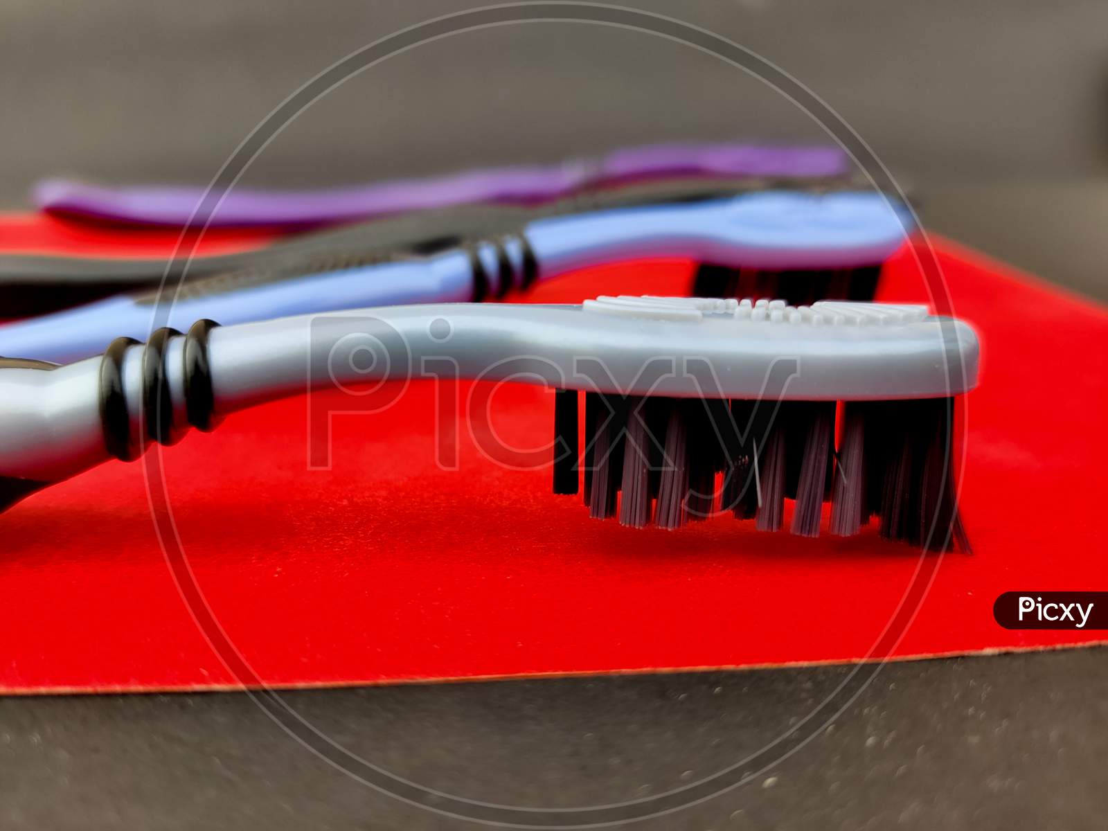 Turn Around Of Grey Tooth Brush With Black Bristle On Red Background