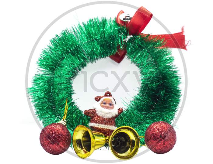 Green Christmas Wreath With Decorations Isolated On White Background, Santa Claus Miniature With Golden Bells And Red Balls