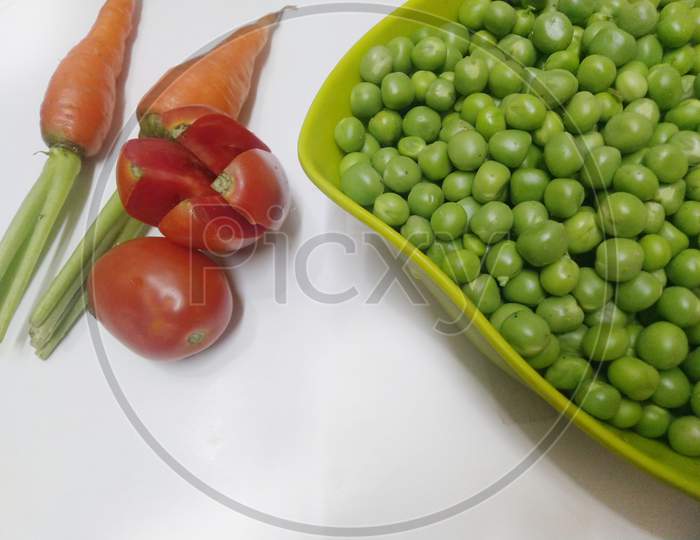 Green peas in a bowl with carrots and tomatoes on white background