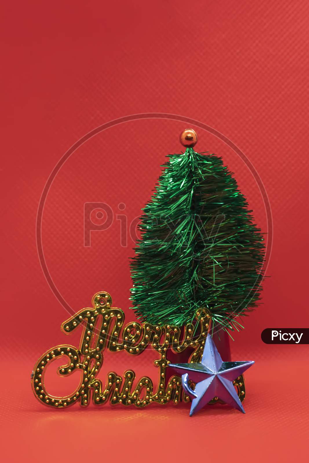 Christmas Tree With Star And Merry Christmas Text On Red Studio Background. Holiday Festive Celebration Greeting Card With Copy Space