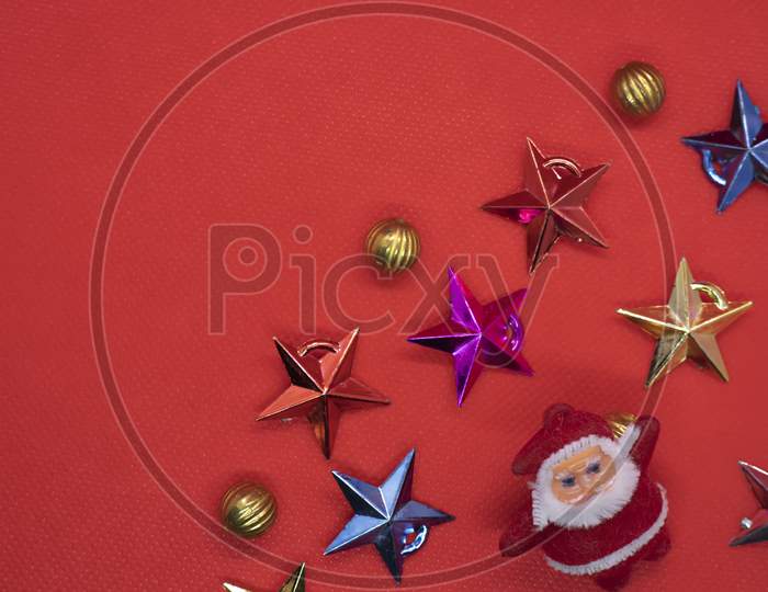 Christmas Composition. Top View Santa Claus Surrounded By Colorful Stars And Christmas Gold Decorations On A Red Background. Flat Lay, Top View, Copy Space