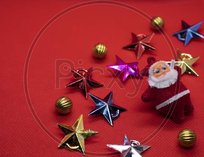 Christmas Composition. Santa Claus Surrounded By Colorful Stars And Christmas Gold Decorations On A Red Background. Flat Lay, Top View, Copy Space