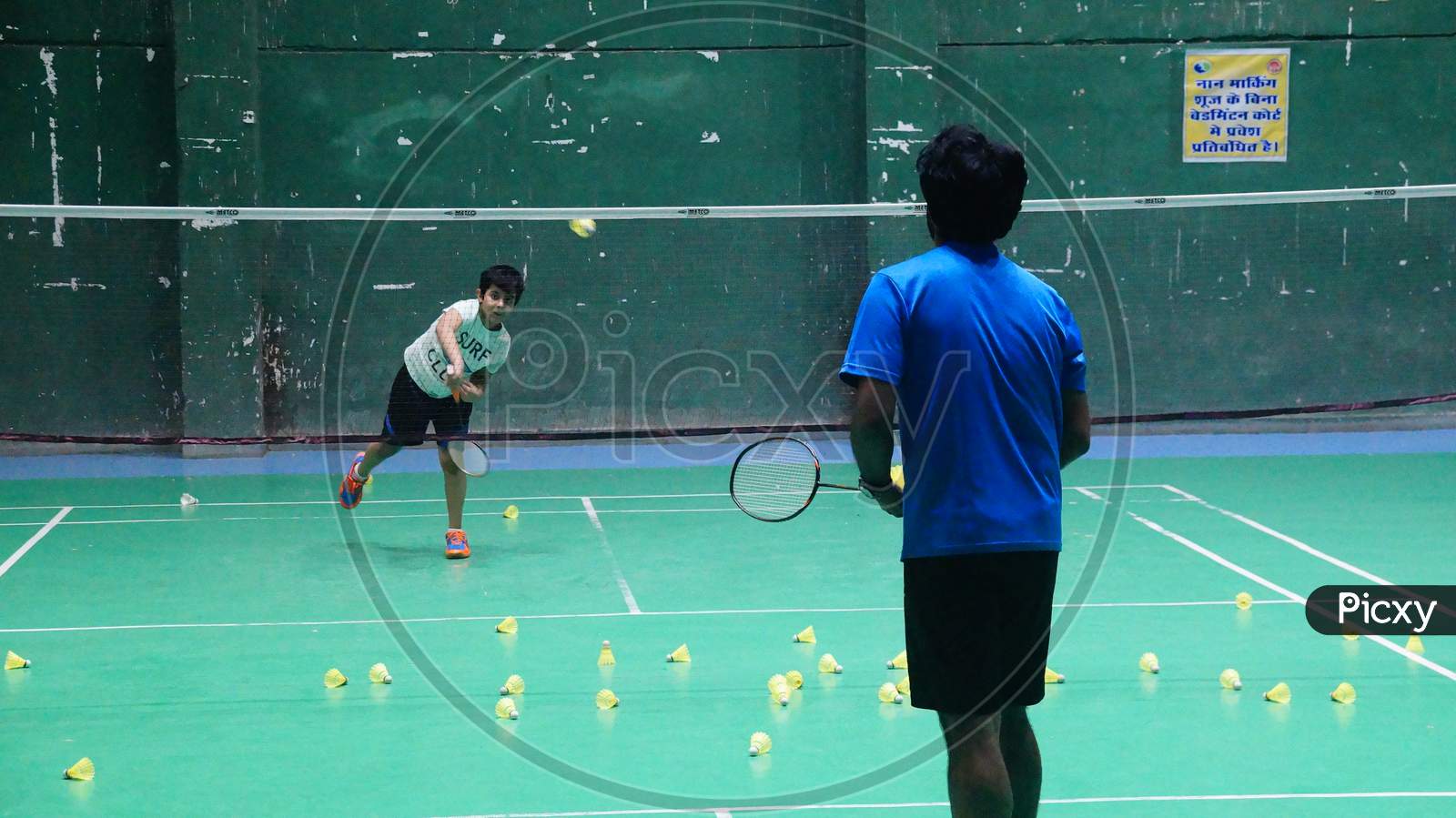 Badminton Trainer feeding shuttlecock while training a beginner badminton player