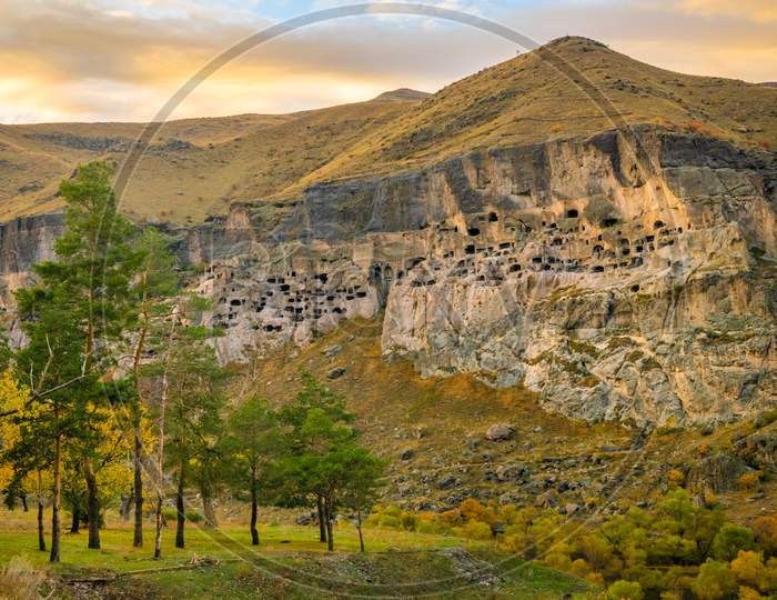 Dramatic Panorama Of Cave City I Vardzia With Trees In Foregound On Autumn Evening During Sunset. Balnk Space Background.
