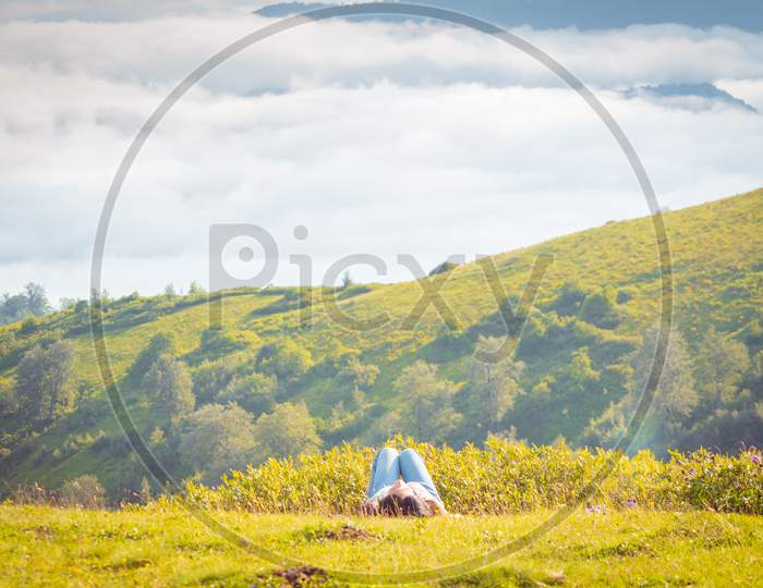 Side View Of Woman Laying Down On The Ground Above The Clouds With Stunning Landscape