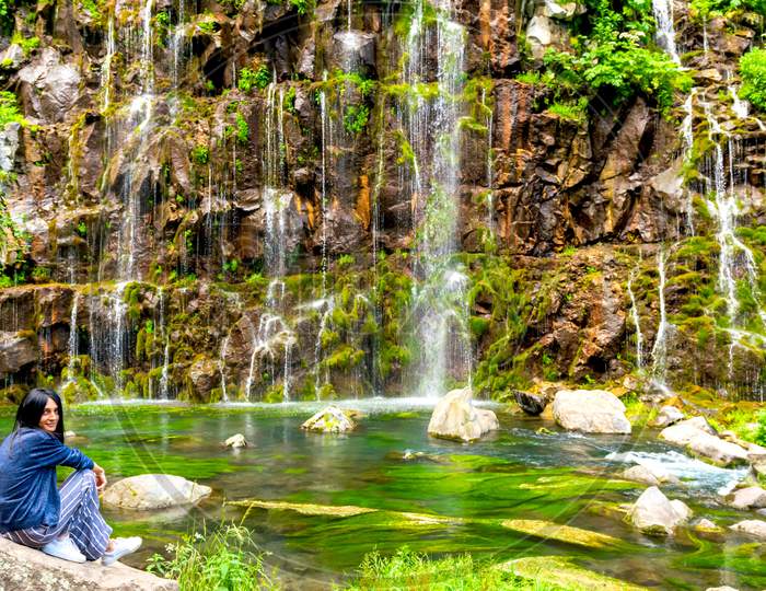Female Tourist Pose With Cascading Waterfall Of Dashbashi Canyon Background. Travel Destination In Caucasus