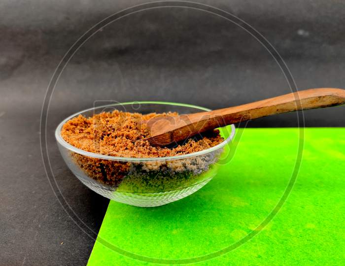 Brown Sugar In Small Glass Bowl With Wooden Spoon. Isolated On Green And Black Background