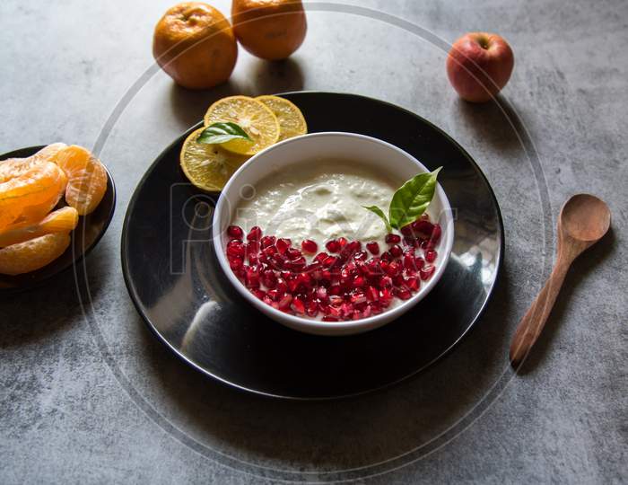 Close up of pomegranate seeds on curd along with fresh fruit ingredients of apples and oranges