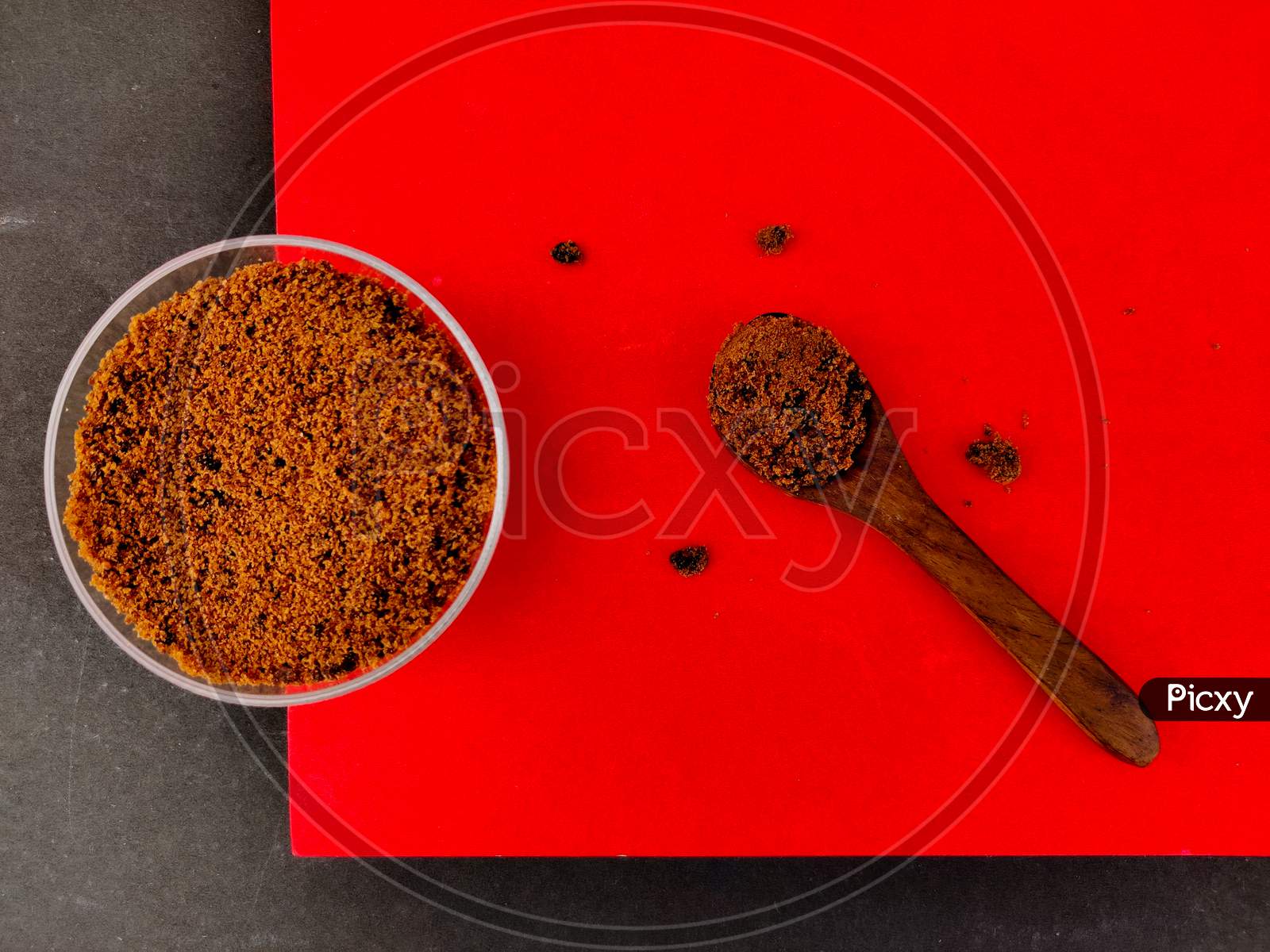 Top View Of Brown Sugar In Small Glass Bowl And Wooden Spoon. Isolated On Red And Black Background