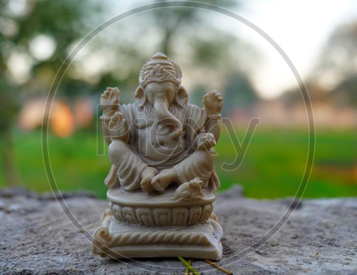 Brown Marble Idol Of Lord Ganesha Isolated On Rough Cement Column With Blurred Background. Christmas Special Concept.