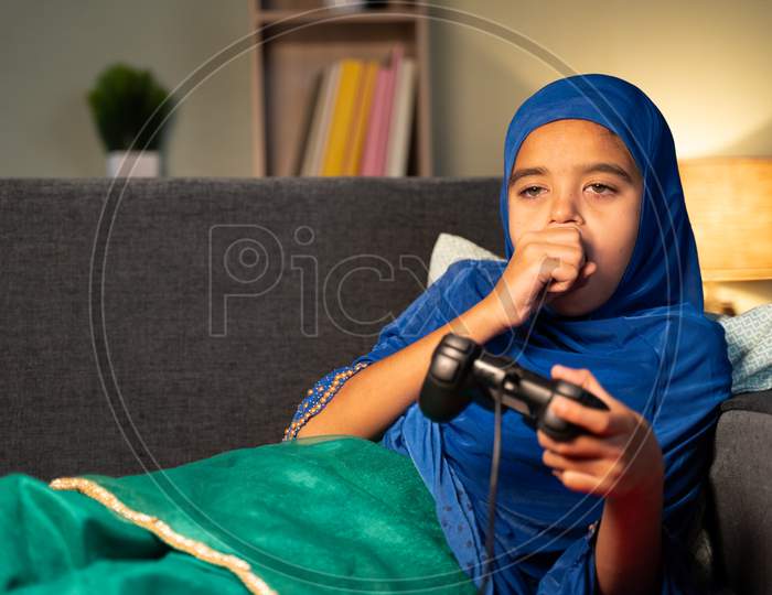 Lazy Muslim Girl Kid Playing Video Game By Using Joystick Or Gamepad At Home While Sleeping On Sofa At Home