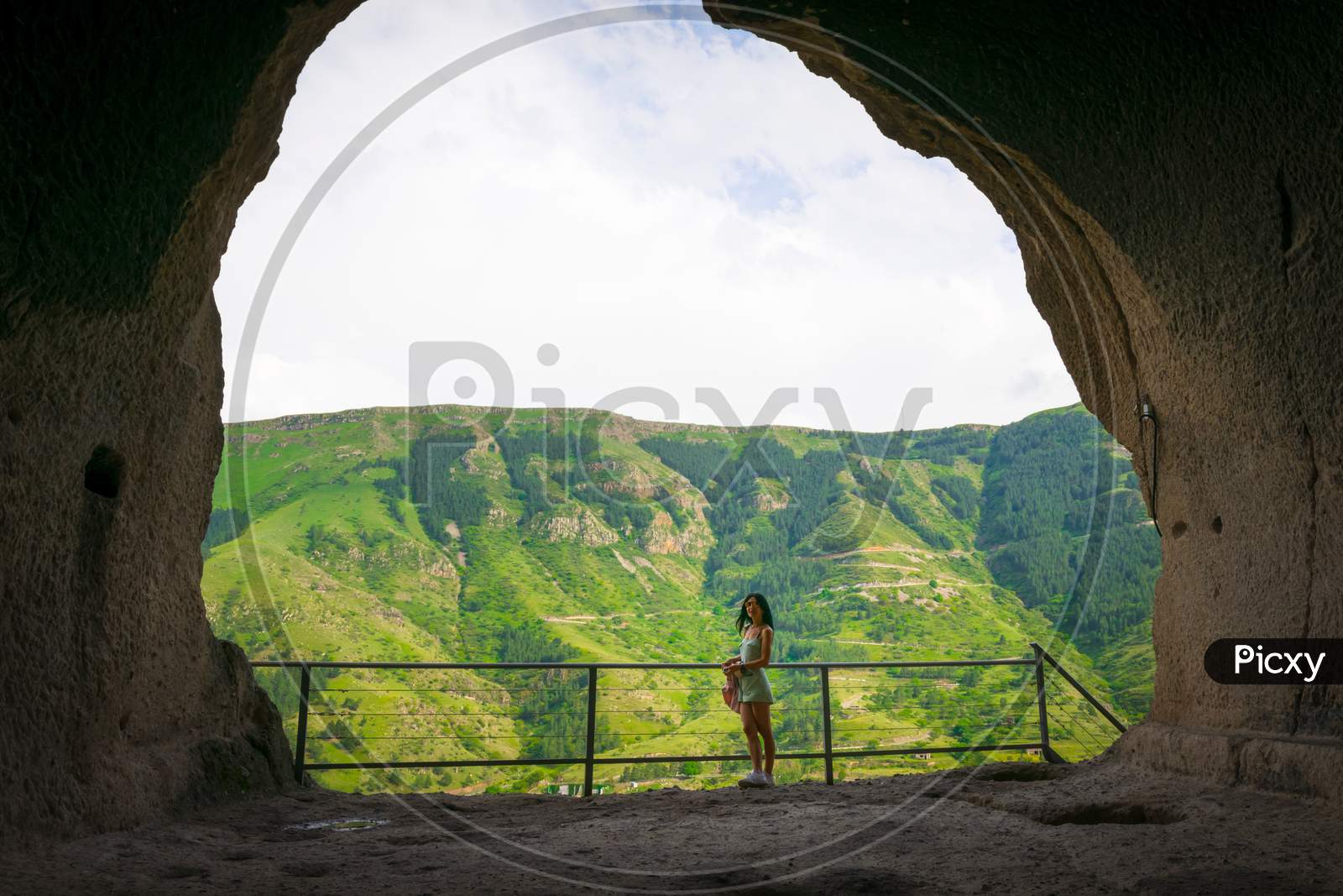 Female Caucasian Tourist Stands In Vadrzia Cave City With Canyon In The Background.