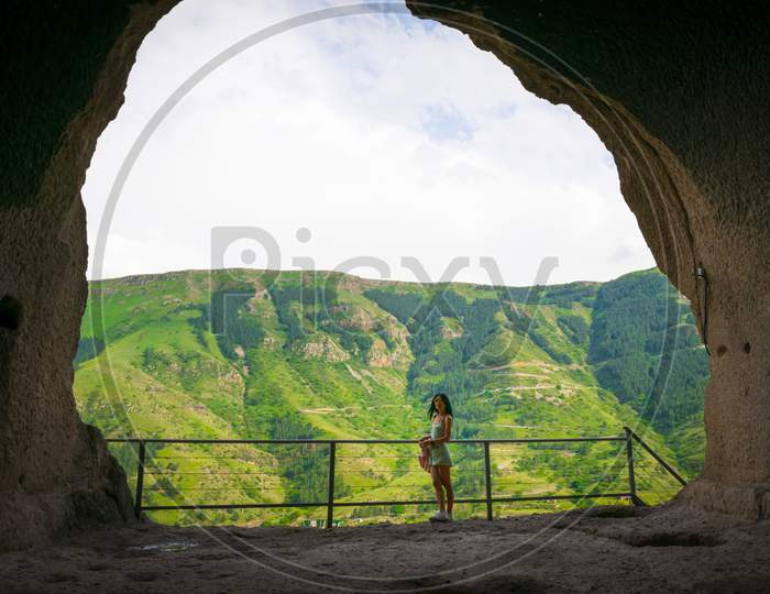 Female Caucasian Tourist Stands In Vadrzia Cave City With Canyon In The Background.