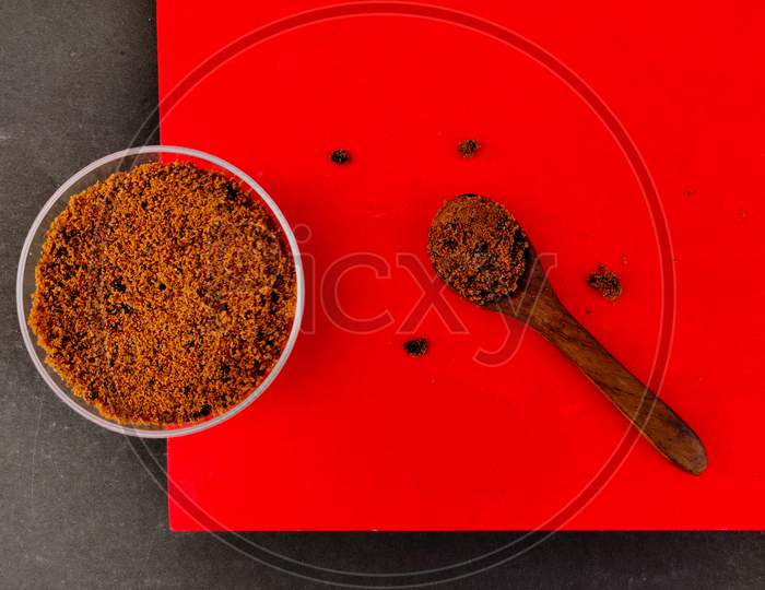 Top View Of Brown Sugar In Small Glass Bowl And Wooden Spoon. Isolated On Red And Black Background