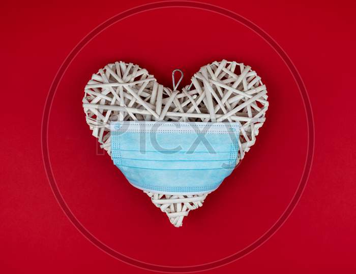 White Heart With A Blue Face Mask On A Red Background. Concept Of A Valentines Day During Coronavirus Or Covid Pandemic.