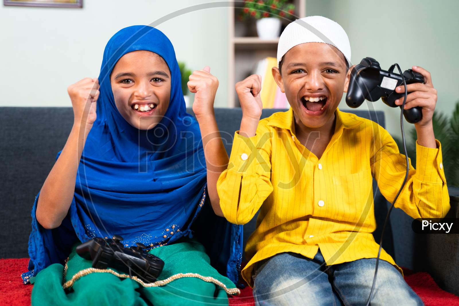Point Of View Shot, Two Muslim Kids Cheering And Shouting After Won The Online Video Game While Playing With Joystick Or Gamepad At Home Sitting On Sofa.