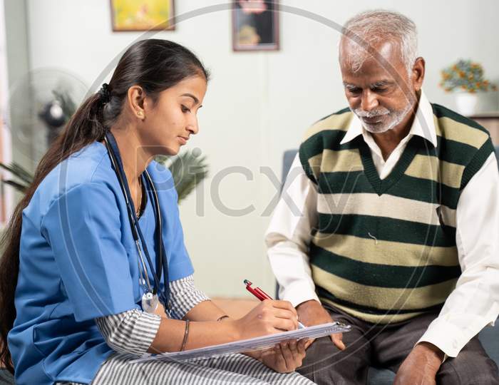 Young Doctor Or Nurse Writing Prescription During Home Medical Service Or Visit To Senior Man.