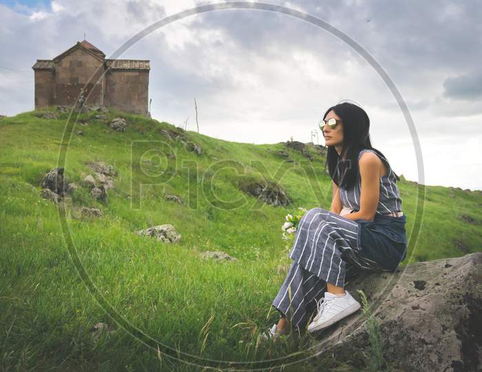 Caucasian Woman Sits On The Rock In Front Of Old Church On The Hill