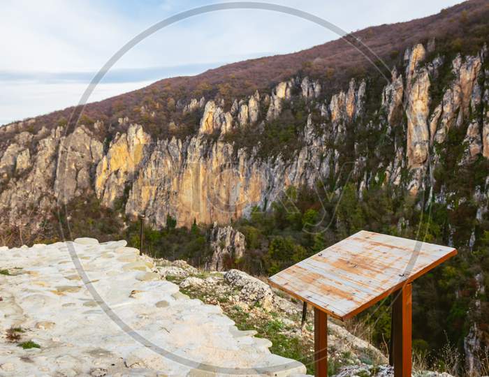 Beautiful View To Eagle Gorge Natural Monument Canyon Cliffs With Blank Wooden Info Stand For Tourist. Travel And Tourism Development In Georgia, Caucasus.