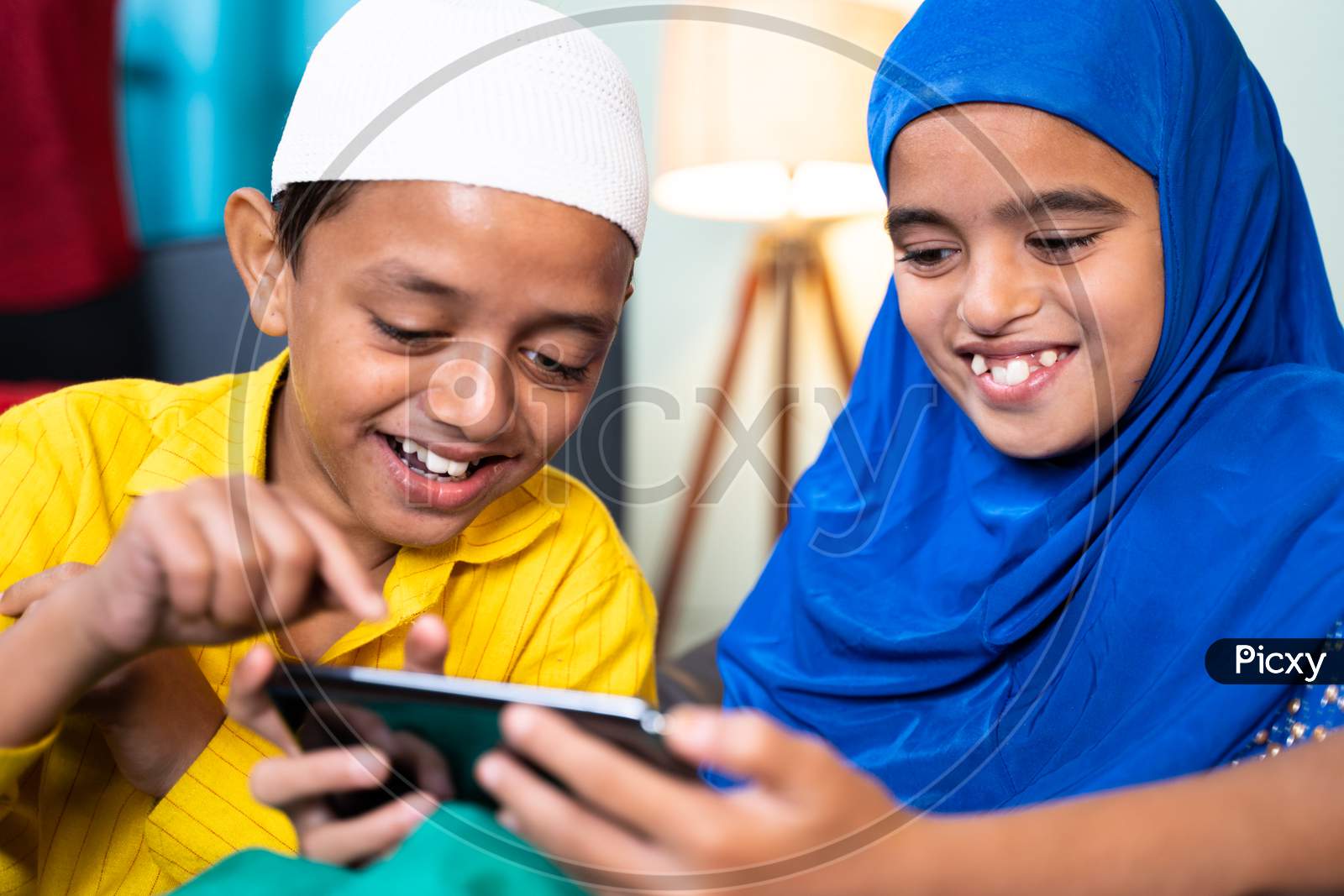 Two Muslim Sibling Kids Busy Using Mobile At Home - Concept Of Kids Using Technology, Internet And Social Media.