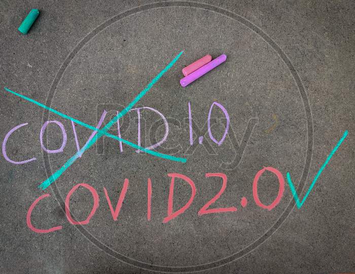 The Inscription Text On The Grey Board, Crossed Out Covid 1.0 And Tick Mark Covid 2.0 Using Color Chalk Pieces.