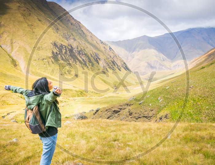 Female Backpacker Stands On The Rock And Enjoys Stunning Mountain Views In Juta Valley. Kazbegi National Park Exploration