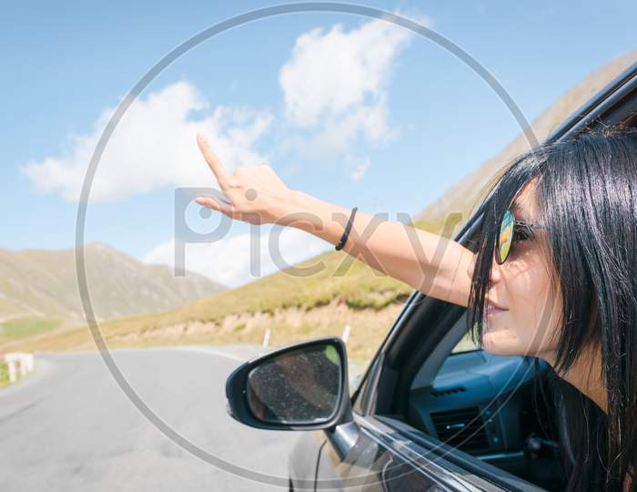 Female Caucasian Woman From Car Window Points Finger Up To Left With Asphalt Road Background. Copypaste Raod Trip Concept.