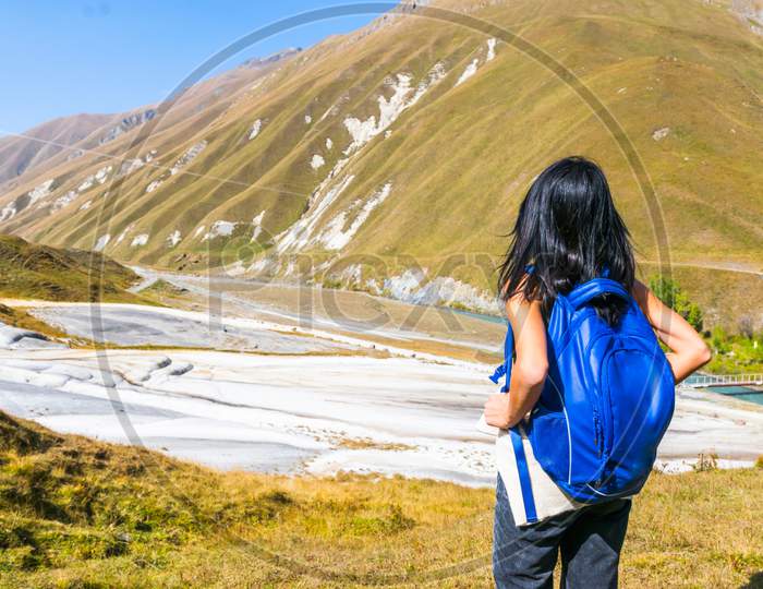 Female Black Hair Woman With Backpack Stands And Looks To White Treventines In Truso Valley. Georgia Travel Destination