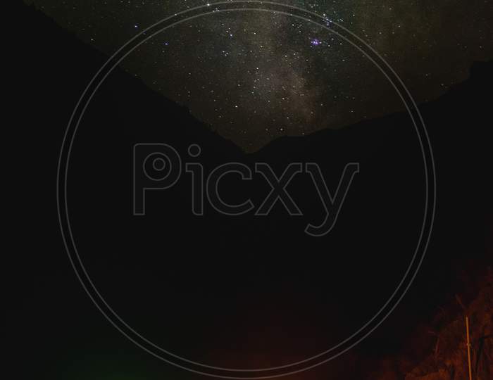 Woman By The Fire With Tent On The Left And Starry Night Landscape With Mountains In Background. Vertical Panorama