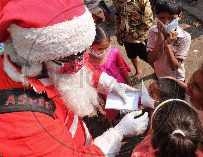 A man wearing a Santa Claus costume puts a mask on a kid, inside a slum, amidst the spread of the coronavirus disease (COVID-19), in Mumbai, India, December, 2020.