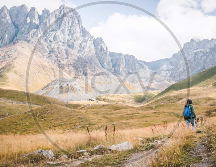 Female Hiker With Backpack On Walks Towards Mountain In A Scenic Juta Valley In Kaznegi National Park.