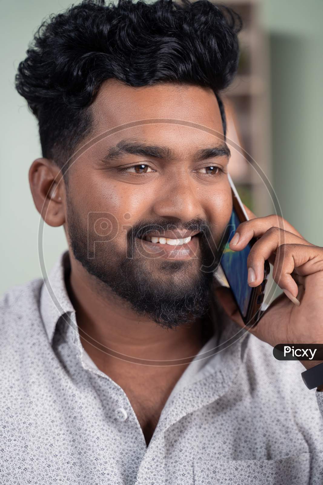 Close Up Of Smiling Young Indian Man Busy Talking Or Having Conversation On Mobile Phone.