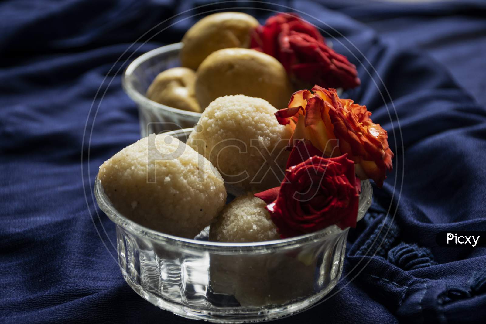 Picture Of Delicious Rawa Laddu Decorated In Bowl With Fresh Red Roses In A Blue Background. Rawa Laddus Made During Diwali Festival In India.