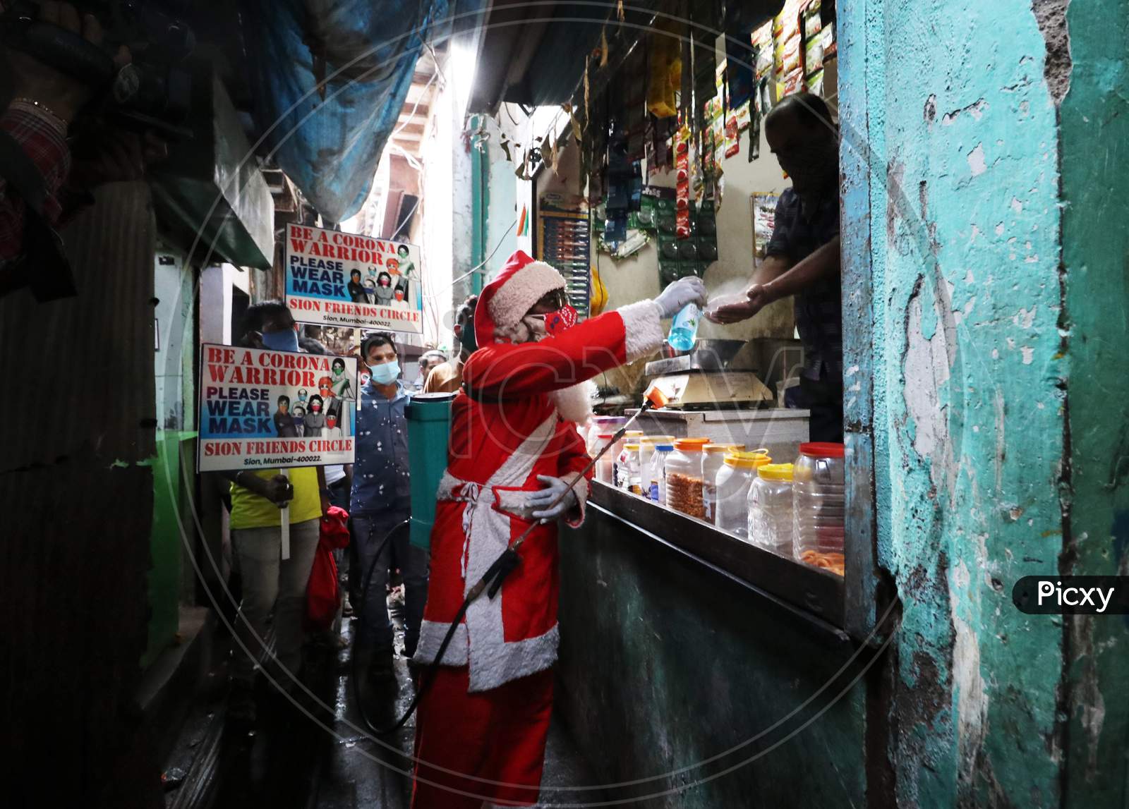 A man wearing a Santa Claus costume sanitizes the hands of a shopkeeper inside a slum, amidst the spread of the coronavirus disease (COVID-19), in Mumbai, India, December, 2020.