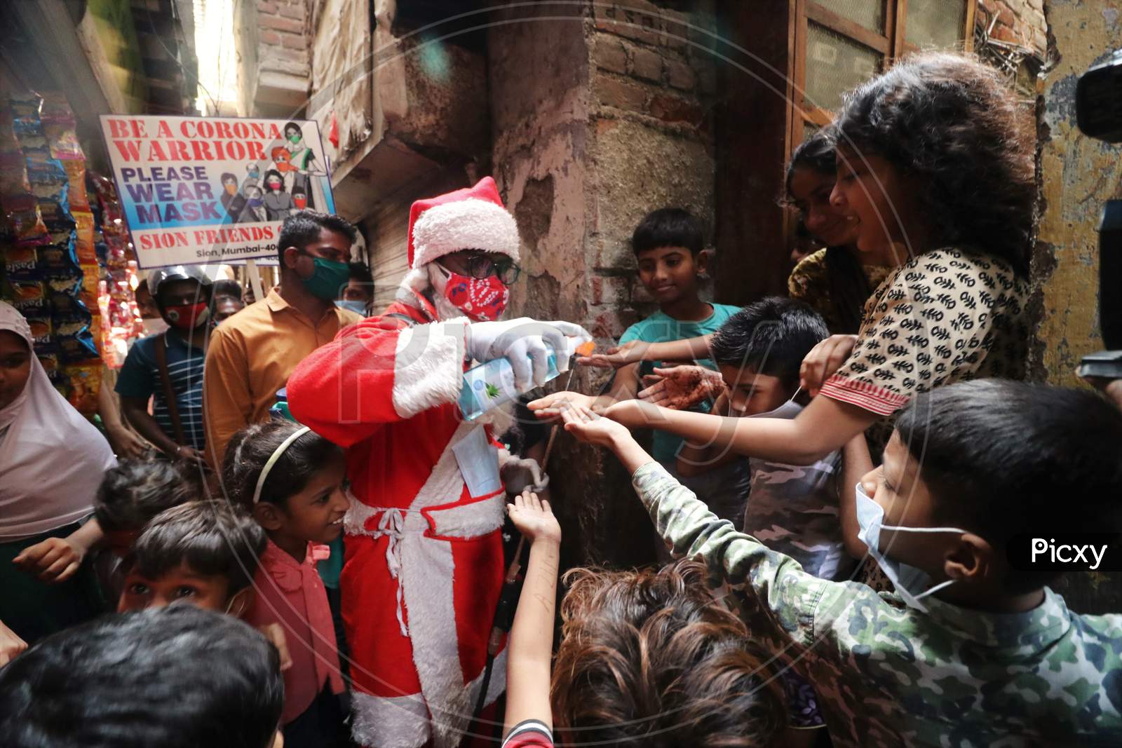A man wearing a Santa Claus costume sanitizes children's hands inside a slum, amidst the spread of the coronavirus disease (COVID-19), in Mumbai, India, December, 2020.