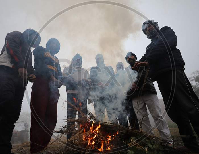 People warm themselves as they stand near the bone fire in a chilli and foggy morning in Jammu,27 Dec,2020.