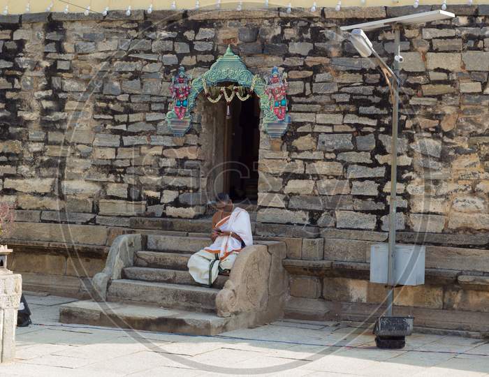A Beautiful picture of an Hindu Priest seen immersed in browsing his smartphone outside the Shiva temple in Talakadu village near Mysuru,India.